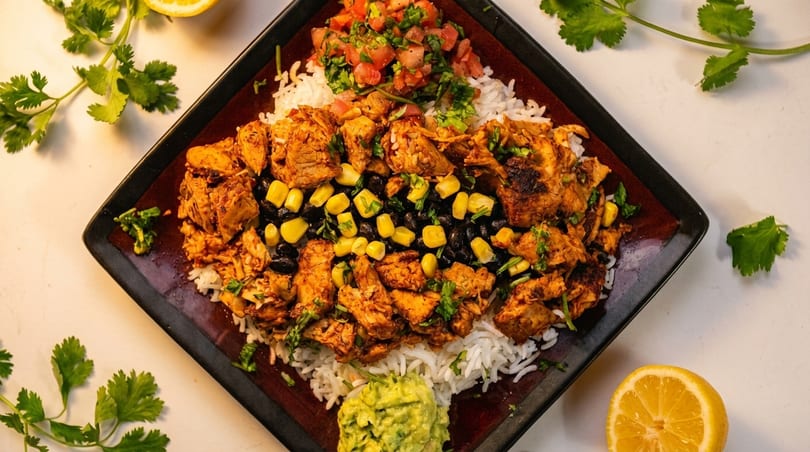 Overhead view of a burrito bowl with chicken, rice, black beans, corn, salsa, and guacamole.