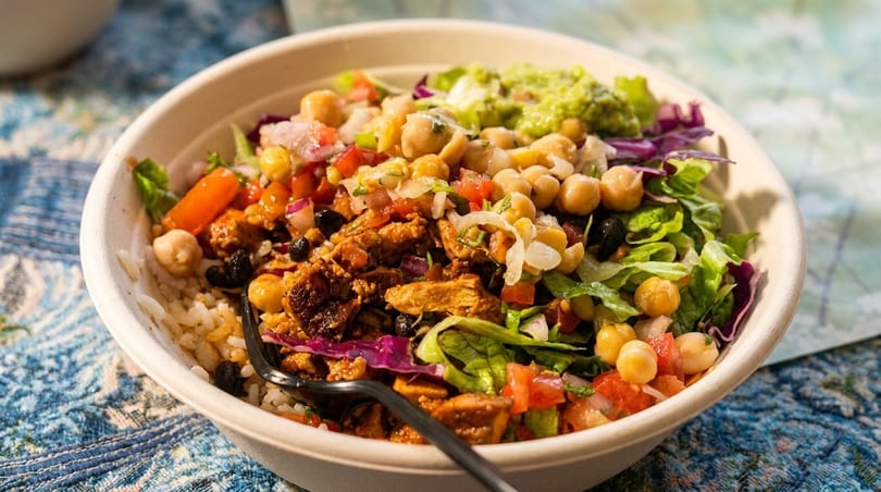 Close-up of a colorful rice bowl with chicken, chickpeas, black beans, salsa, and guacamole.